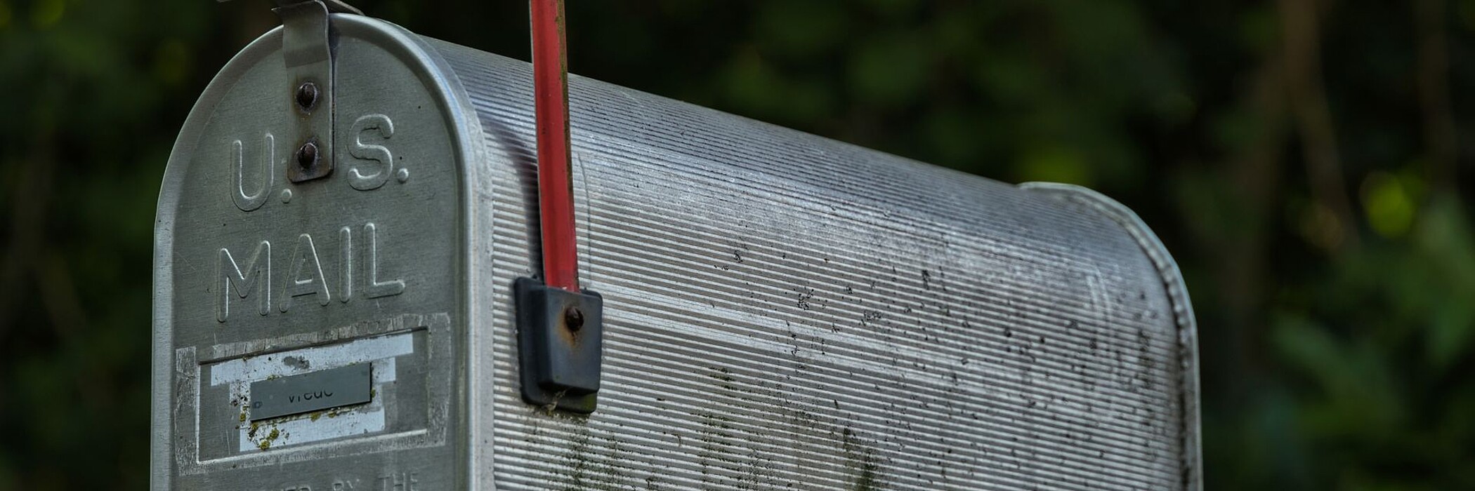Grauer US-Postkasten mit roter Flagge an einem Holzzaun.